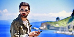 Ο Ανδρέας Γεωργίου κρατάει το κινητό του με φόντο τη θάλασσα