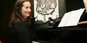 H Ελένη Καραΐνδρου κάθεται στο πιάνο και χαμογελάει