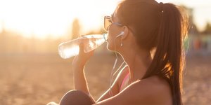 Γυναίκα πίνει νερό στην παραλία με ακουστικά στα αυτιά