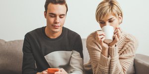 Γυναίκα πίνει τον καφέ της και κοιτάζει το κινητό του φίλου της με καχυποψία