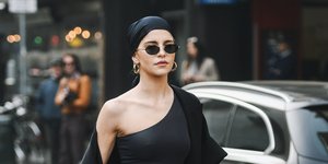 Γυναίκα περπατάει φορώντας μαύρα γυαλιά, μαύρο τοπ με έναν ώμο έξω και λευκό παντελόνι.