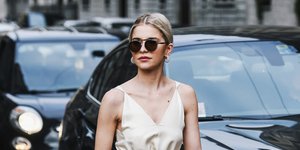 Γυναίκα με μπεζ φόρεμα και γυαλιά ηλίου περπατάει στον δρόμο