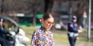 Γυναίκα στους δρόμους της πόλης με εμπριμέ φόρεμα, λευκά μποτάκια και λευκή τσάντα