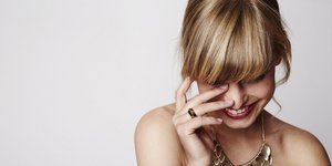 Ξανθιά γυναίκα με κόκκινο κραγιόν, λευκό τοπ και χρυσό κολιέ χαμογελά