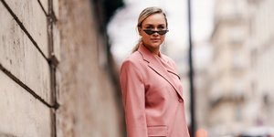 Γυναίκα με ροζ κοστούμι και ψάθινη τσάντα στέκεται όρθια