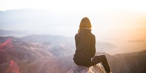 Γυναίκα κάθεται σε βράχο και κοιτάζει τη θέα από ψηλά