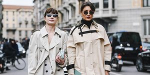 Δύο γυναίκες με καμπαρντίνες και γυαλιά ηλίου περπατούν στον δρόμο