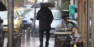 Ενας άνδρας περπατά στη βροχή κρατώντας ομπρέλα