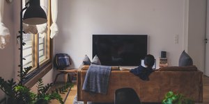 Γυναίκα κάθεται σε καναπέ καθιστικού μπροστά στην τηλεόραση 