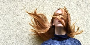 Μια γυναίκα με μακριά ξανθά μαλλιά και μπλε μπουφάν μπροστά σε τοίχο