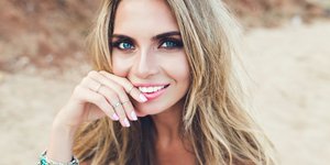 Μια ξανθιά γυναίκα χαμογελάει με μπλε μάτια και δαχτυλίδια στα δάχτυλα