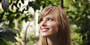 Ξανθιά γυναίκα με γαλάζια μάτια χαμογελά σε έναν κήπο