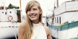 Ξανθιά γυναίκα με μακριά μαλλιά και λευκή μπλούζα στο λιμάνι 