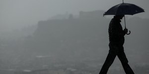Ενας άνδρας περπατά κρατώντας ομπρέλα, μια βροχερή ημέρα στην Αθήνα