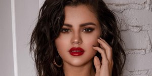 Η Σελένα Γκόμεζ με κόκκινο μαγιό και κόκκινα χείλη, πιάνει το μάγουλό της