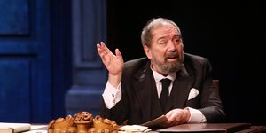 Ο Σταμάτης Φασουλής καθισμένος στο γραφείο φορώντας μαύρο κοστούμι και γραβάτα 