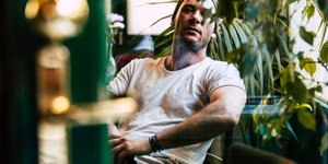 O Aντίνοος Αλμπάνης με λευκό T-Shirt καθισμένος ποζάρει στο φακό