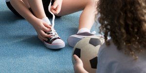 Ενα αγόρι δένει τα κορδόνια του, ένα κορίτσι κρατά μια μπάλα ποδοσφαίρου