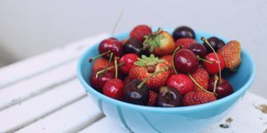 Ενα μπλε μπολ με κεράσια και φράουλες σε λευκό ξύλινο τραπέζι