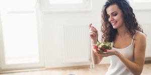 Μελαχρινή γυναίκα χαμογελάει και τρώει μια σαλάτα