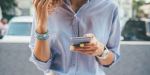 Γυναίκα με πουκάμισο και τζιν, κρατά κινητό με κίτρινα νύχια 