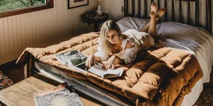 Μια γυναίκα σε κρεβατοκάμαρα διαβάζει βιβλίο πάνω στο κρεβάτι