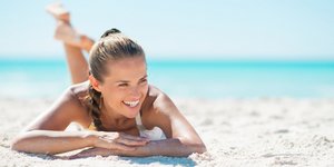 Γυναίκα ξαπλωμένη στην παραλία με μαγιό χαμογελάει