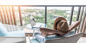 Γυναίκα με καπέλο κάθεται στη βεράντα με το λάπτοπ της