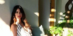 H Ηλιάνα Παπαγεωργίου φοράει μακρύ ριγέ φόρεμα και κάθεται σε λευκό πάγκο