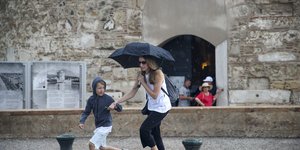 Γυναίκα και παιδί τρέχουν στη βροχή κρατώντας ομπρέλα