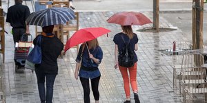Τρεις γυναίκες περπατούν σε παλαιότερη καλοκαιρινή βροχή, κρατώντας ομπρέλες