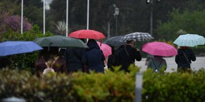 Κόσμος κρατάει ομπρέλες και περπατάει