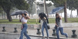 Κόσμος περπατάει με ομπρέλες στη βροχή
