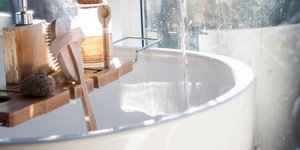 Μια λευκή μπανιέρα, ένας ξύλινος δίσκος, αξεσουάρ μπάνιου, παράθυρο