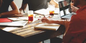Μια παρέα κάθεται σε ένα τραπέζι με υπολογιστή, ποτήρι, σημειώσεις