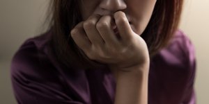 Γυναίκα με μοβ μπλούζα ακουμπάει το πιγούνι της και έχει αγωνία