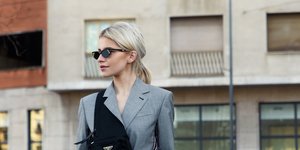 Γυναίκα με γκρι κοστούμι, μαύρα γυαλιά και μαύρη τσάντα 