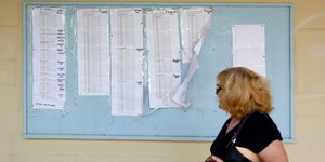 Μια γυναίκα περνά μπροστά από πίνακες στους οποίους έχουν αναρτηθεί βάσεις εισαγωγής