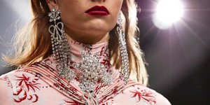 Μοντέλο με κόκκινο κραγιόν, κρεμαστά σκουλαρίκια και ροζ φόρεμα με prints στην πασαρέλα