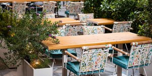 H αυλή του Local Green με ξύλινα τραπέζια, λευκές καρέκλες και φυτά