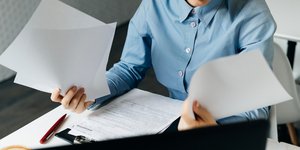 Γυναίκα με μπλε πουκάμισο πιάνει πολλά χαρτιά στο γραφείο της
