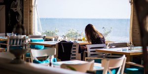 Γυναίκα κάθεται μόνη της σε ένα εστιατόριο με θέα τη θάλασσα