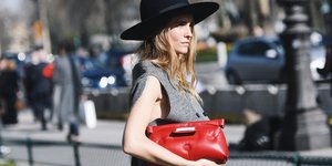 Μια γυναίκα με μαύρο καπέλο, γιλέκο και κόκκινη τσάντα