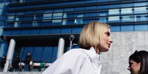 Μια γυναίκα με ξανθά μαλλιά, λευκό πουκάμισο και ροζ παντελόνι