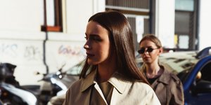 Μια γυναίκα με μακριά καστανά μαλλιά και trench coat περπατά στο δρόμο