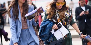 Μια γυναίκα με μπλε κοστούμι και λευκά και μια γυναίκα με πράσινη φούστα και μαύρα μποτάκια