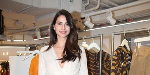 H Ηλιάνα Παπαγεωργίου με λευκό φόρεμα και μαύρα πέδιλα μπροστά από ρούχα