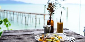 Πιάτο με ψάρι και λαχανικά πάνω σε τραπέζι με θέα τη θάλασσα