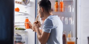 Αντρας τρώει μπροστά από ψυγείο