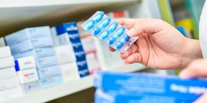 Χέρια κρατούν καρτέλα με χάπια μπροστά σε ράφι φαρμάκων